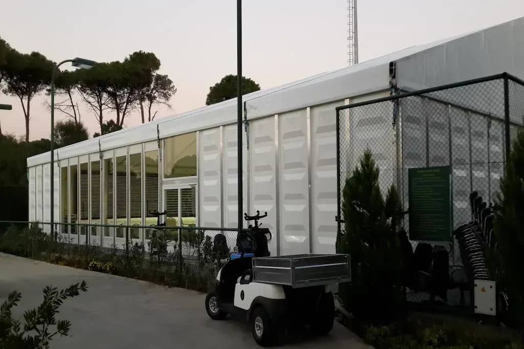 Çamlar arasında cam cepheli uzun çadır ve önündeki golf arabası