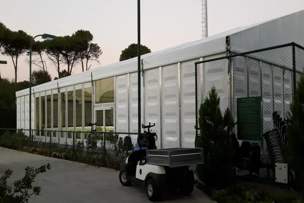 Çamlar arasında cam cepheli uzun çadır ve önündeki golf arabası