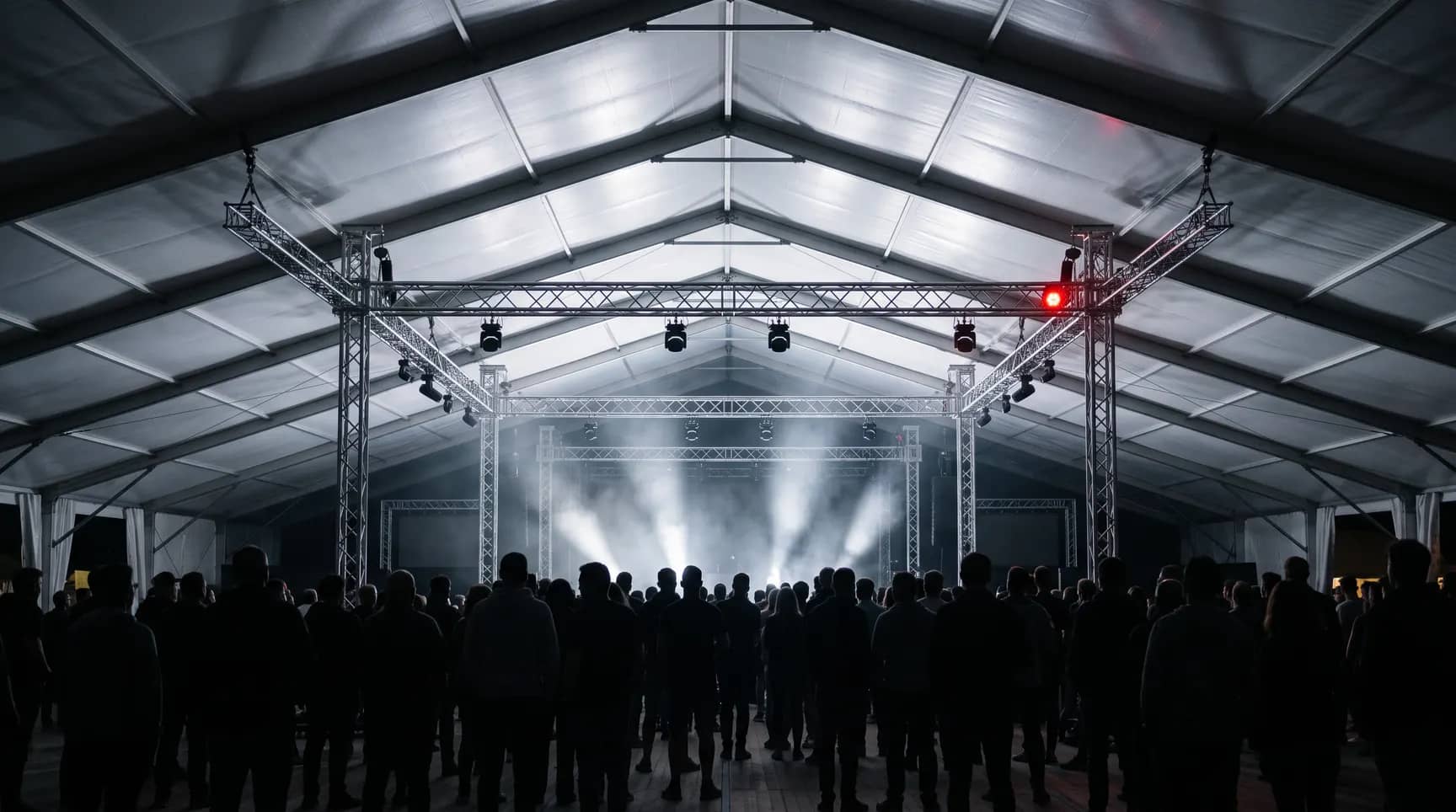 Gece festival çadırı: sahne trussları, ışık demetleri ve seyirci siluetleri