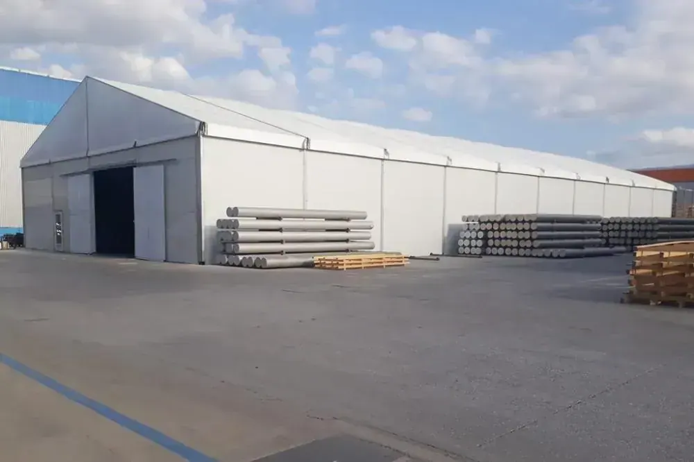 Sanayi sahasında geniş açıklıklı beyaz depo çadırı ve önünde istiflenmiş malzeme