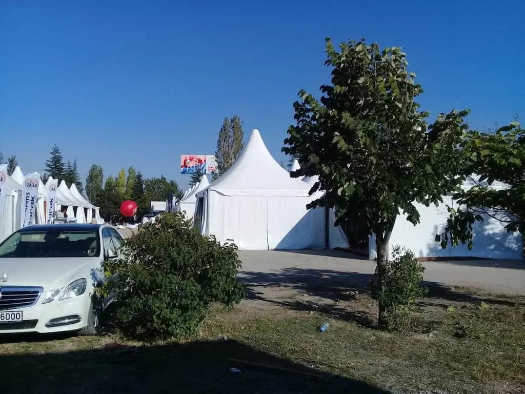 Ağaçlık alanda kurulmuş pagoda çadırları ve önünde sergilenen araç