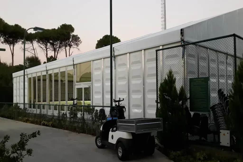 Çamlar arasında cam cepheli uzun çadır ve önündeki golf arabası