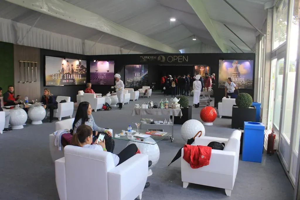 Turnuva çadırında beyaz koltuklu lounge alanı ve ekranlar