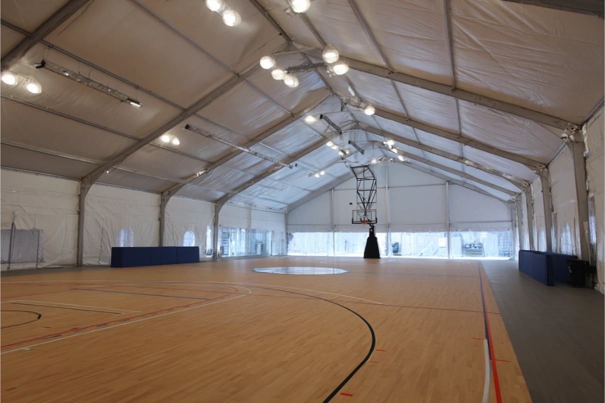Büyük çadır içinde parkeli basketbol sahası, pota ve duvar koruma minderleri