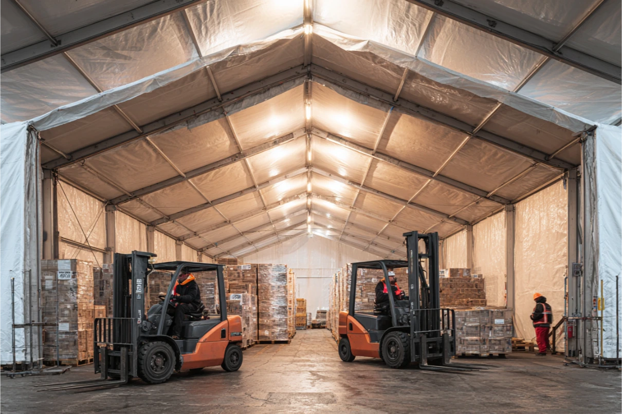 Depo çadırı içinde iki forklift ve iki yana istiflenmiş paletli yükler