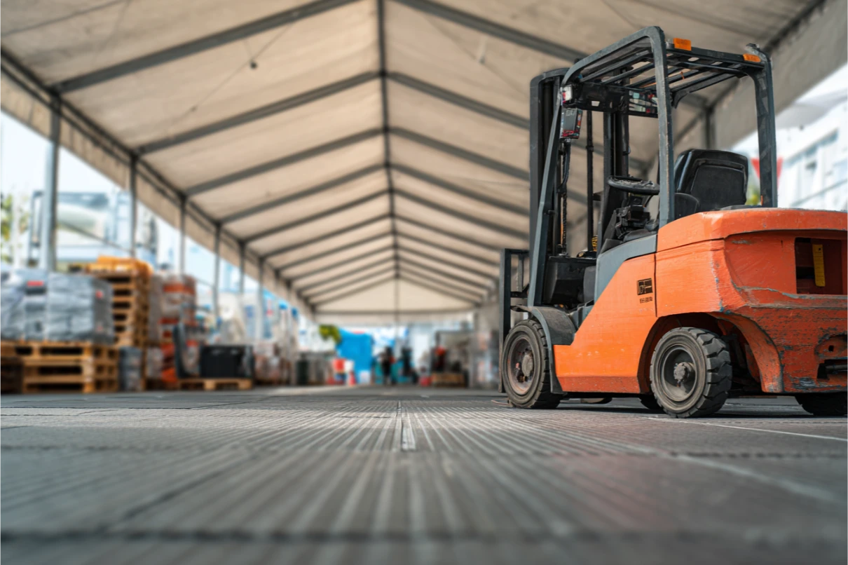 Çadır içinde çelik podyum zemin üzerinde duran forklift ve yanında palet istifleri