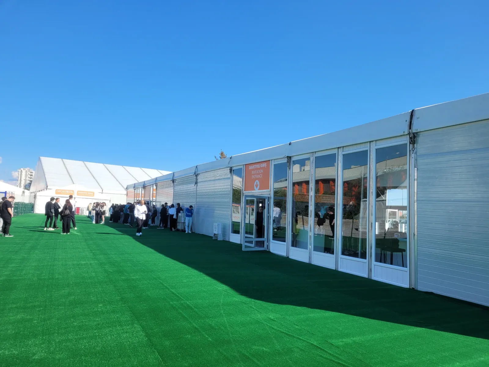 Cam kapılı fuar çadırı cephesi boyunca yürüyen Growtech Antalya ziyaretçileri